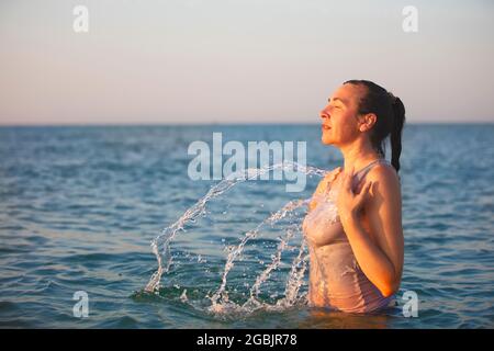 Une femme d'âge moyen se tient dans la mer et éclabousse l'eau. Banque D'Images