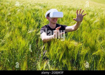 Homme utilisant des lunettes de réalité virtuelle à l'extérieur dans la nature sur un champ de culture du blé. Banque D'Images