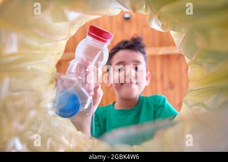 image de l'intérieur d'un bac de recyclage avec un sac jaune d'un enfant qui jette une bouteille en plastique pour recycler dans lequel le visage de l'enfant est hors foyer Banque D'Images