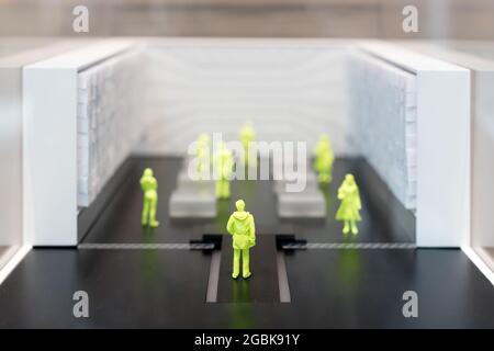 Groupe de personnes miniatures jaunes social distancer dans une salle avec foyer sélectif à l'arrière d'une figure masculine dans le premier plan et l'espace de copie Banque D'Images