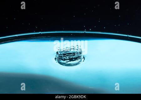 Projection d'eau en forme de couronne et chute. Projection des gouttes d'eau qui tombent. Goutte d'eau sur fond bleu. Surface d'eau bleue avec éclaboussures. CLE Banque D'Images