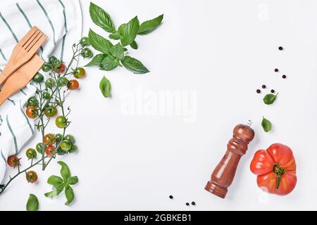 Branches de tomates cerises fraîches, feuilles de basilic, serviette, poivre et moulin à poivre sur fond blanc. Fond de cuisine et maquette. Banque D'Images