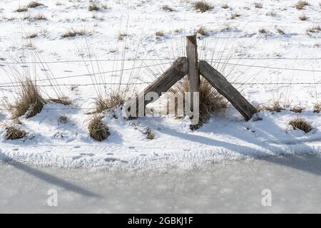 Photo en grand angle de clôtures en bois sur le terrain enneigé par une journée ensoleillée Banque D'Images