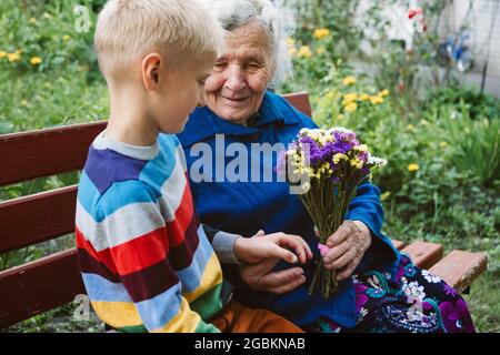 Réunis, famille, ensemble, relations, réunion, s'embrasser. Visite de petit-fils la grand-mère donne des fleurs après une longue pause due au coronavirus Banque D'Images