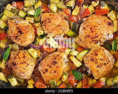 Cuisses de poulet, courgettes et légumes cuits dans un plat de cuisson sur une table sombre. Vue de dessus, au-dessus de la tête Banque D'Images