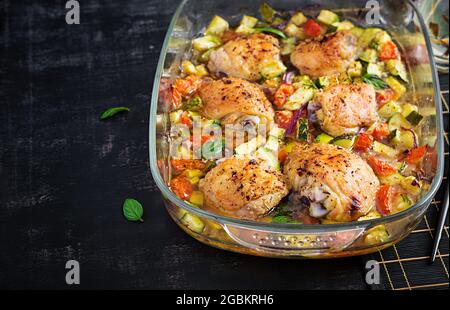 Cuisses de poulet, courgettes et légumes cuits dans un plat de cuisson sur une table sombre. Banque D'Images