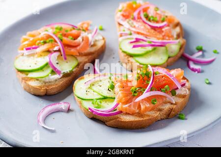 Toasts au fromage à la crème, saumon fumé, concombre et oignon rouge sur table rustique en bois. Sandwichs ouverts. Soins de santé, concept de super alimentation. Banque D'Images