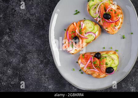 Toasts au fromage à la crème, saumon fumé, concombre, olives noires et oignon rouge. Sandwichs ouverts. Soins de santé, concept de super alimentation. Vue de dessus, au-dessus de la tête Banque D'Images