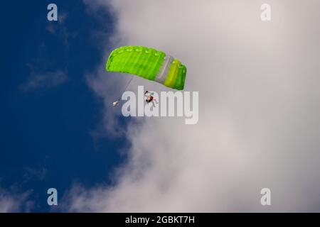 Skydiver sous la verrière verte du parachute contre un ciel bleu et des nuages blancs Banque D'Images