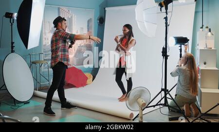 Arrière-plan de la photo: Assistant de réglage du projecteur pendant que le photographe prend des photos de modèle noir joli Banque D'Images