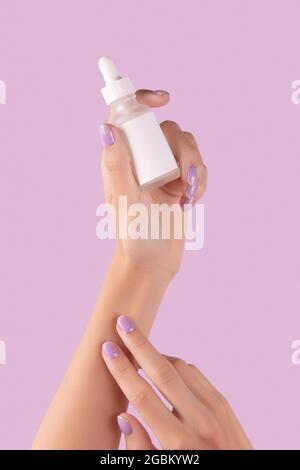 Les femmes tiennent main compte-gouttes avec du sérum sur fond de lavande pastel Banque D'Images