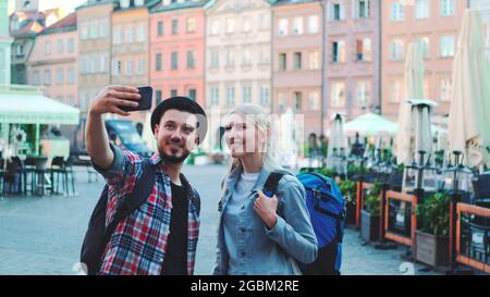 Un couple heureux de jeunes touristes qui font du selfie sur smartphone dans le centre-ville. Ils ont des sacs de touristes. Banque D'Images