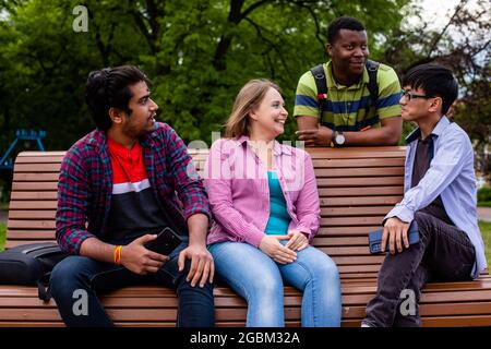 Joyeuse compagnie diversifiée d'amis d'université sur banc en bois Banque D'Images