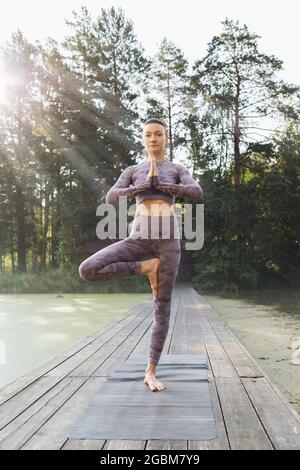 Une femme pratiquant le yoga, le matin sur un pont en bois dans le parc, exécute l'exercice vrikshasana, pose d'arbre Banque D'Images