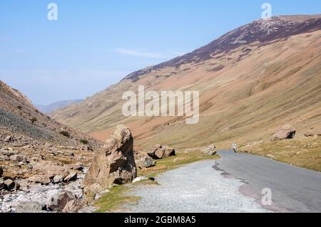 Un cycliste grimpe une ruelle de campagne étroite à travers le col Honister sous les montagnes du Lake District d'Angleterre. Banque D'Images