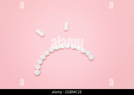 Préjudice pharmaceutique. Angry Smiley visage fait de pilules blanches, couché sur le Backgrond rose. Industrie pharmaceutique mondiale et médicaments Banque D'Images