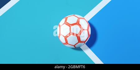 Gros plan d'un ballon futsal orange blanc dans le coin d'un fond bleu vif de terrain de football Banque D'Images