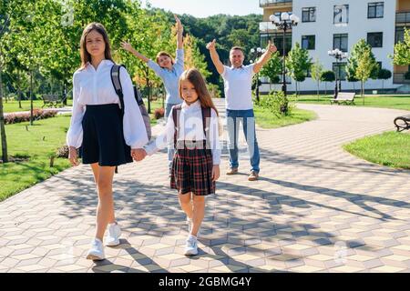 Deux sœurs filles tiennent la main et vont à l'école pendant que leurs parents se réjouissent Banque D'Images