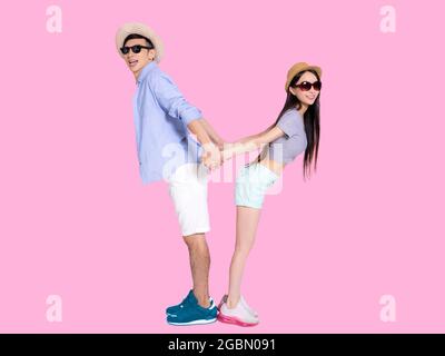 Jeune couple en lunettes de soleil et debout dos à dos. Isolé sur fond rose. Banque D'Images