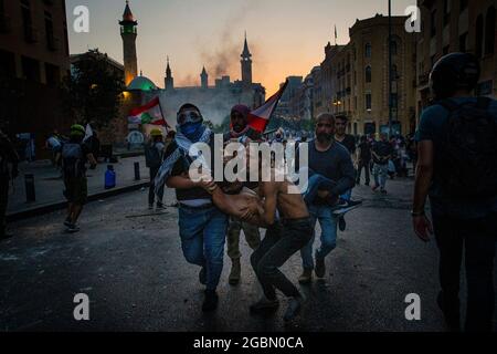 Beyrouth, Beyrouth, Liban. 4 août 2021. Les manifestants portent un manifestant blessé lors d'une manifestation antigouvernementale à l'occasion de l'anniversaire de l'explosion portuaire de Beyrouth, au Liban, le 4 août 2021. La Croix-Rouge libanaise a signalé que 10 personnes avaient été blessées et transportées dans des hôpitaux à la suite d'affrontements dans le centre-ville de Beyrouth, et que 71 personnes avaient été soignées sur les lieux. L'explosion, l'une des plus grandes explosions non nucléaires de l'histoire humaine, a détruit des marais de la ville, tué au moins 218 personnes, blessé des milliers et déplacé environ 300,000 personnes. Un an plus et il n'y a pas eu de ca Banque D'Images