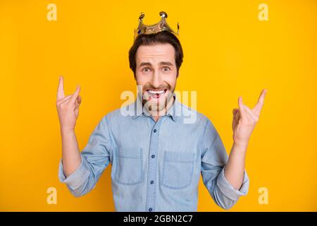 Photo du jeune homme excité heureux sourire positif montrer rock signe couronne roi isolé sur fond jaune de couleur Banque D'Images