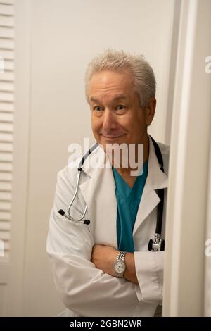 Beau médecin mature souriant loin de la caméra avec les bras croisés portant le stéthoscope Banque D'Images