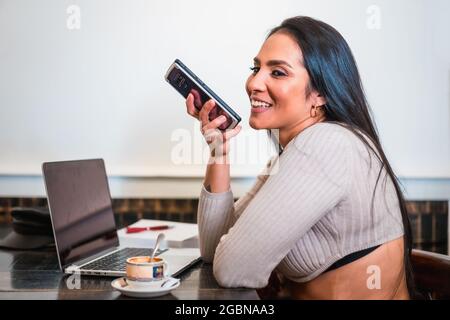 Gros plan d'une jeune Latina assis dans un café souriant et parlant au téléphone pendant une pause café Banque D'Images