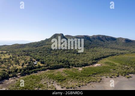 Survoler des mangroves sur la plage à marée basse et vers une chaîne de montagnes boisées et une maison isolée Banque D'Images