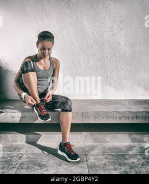 Faites de l'exercice femme asiatique active se préparer à courir portant des chaussures de course sur un banc de gym à la maison en utilisant la technologie SmartWatch. Athlète sportif Banque D'Images