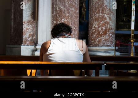 La lumière divine et dorée traverse une fenêtre et brille sur un adorateur dans une église locale. À Rome, Italie. Banque D'Images