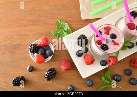 Smoothie aux fruits de la forêt avec du lait dans des verres en verre sur une assiette blanche et des fruits sur un banc en bois. Vue de dessus. Banque D'Images