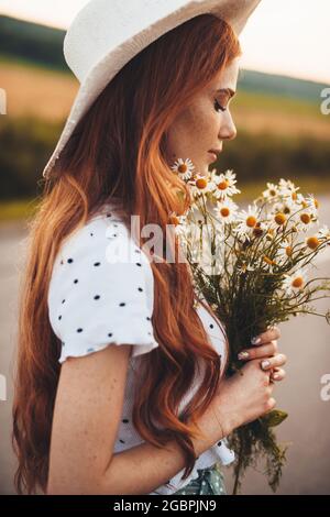 Gros plan d'une femme au gingembre avec des taches de rousseur tenant un bouquet de fleurs portant un chapeau dans le champ Banque D'Images