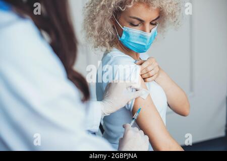 Une femme blonde se fait vacciner dans un centre de santé portant un masque médical Banque D'Images