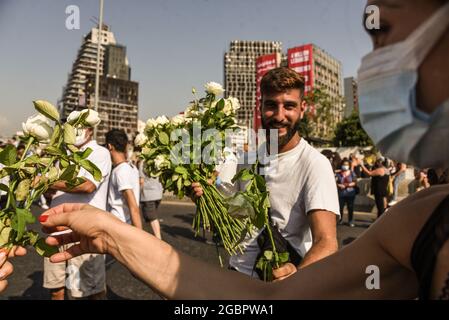 Beyrouth, Liban, le 4 août 2021. Un homme remet des fleurs aux personnes protestant contre l'échec à trouver les responsables du Blast de Beyrouth et les tient pour responsables devant les bâtiments endommagés par l'explosion, encore non réparés un an plus tard. Banque D'Images