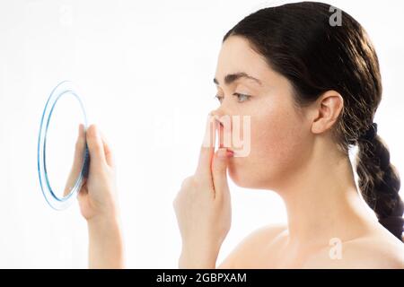 Chirurgie du nez en plastique. Portrait de la jeune femme caucasienne touchant son nez crocheté et regarde le miroir, isolé sur fond blanc. Concept de rh Banque D'Images