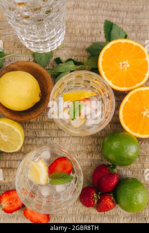 Vue de dessus de deux grands verres avec glace à l'eau et fraise. Tranches de fruits frais sur la table à l'extérieur. Citron vert et orange. Concept alimentaire Banque D'Images