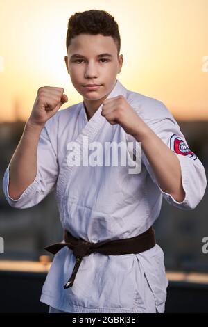 Jeune adolescent karaté praticien en kimono blanc entraînement sur le toit au coucher du soleil Banque D'Images