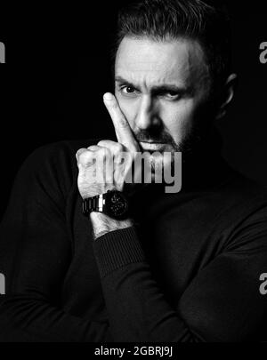 Noir et blanc. Portrait d'un homme concentré non rasé en col roulé noir, pull tenant la main au menton, à la barbe et à la joue Banque D'Images