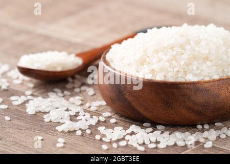 Riz comestible blanchi blanc brut poli sur fond de table en bois dans un bol, concept de conception biologique. Banque D'Images