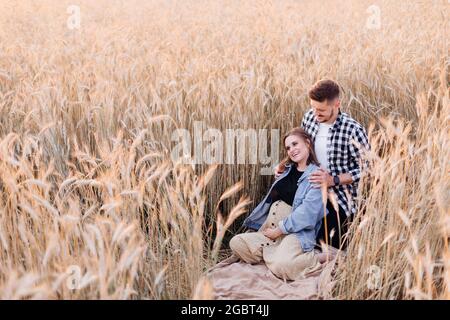 Le jeune couple enceinte apprécie la nature le soir d'été dans le champ parmi les plantes céréalières. Famille et grossesse. Amour et tendresse. Bonheur et sérénité. Banque D'Images