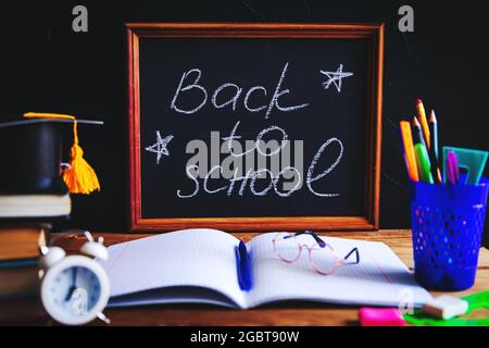 Livres, matériel d'écriture, lunettes, bloc-notes et réveil sur le bureau. Lettrage « Back to School ». Concept d'apprentissage et d'auto-éducation. Séle Banque D'Images