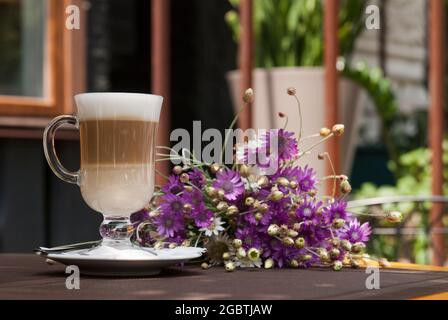 Verre de latte et fleurs violettes sur la terrasse d'été du restaurant Banque D'Images
