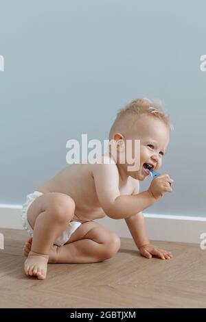 un petit garçon brosse ses dents avec une brosse à dents et rit, sur fond de mur bleu Banque D'Images