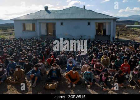 03 août 2021, Turquie, Çaldiran: Environ 400 réfugiés d'Afghanistan, du Pakistan et d'Iran, pris en charge par la police turque, attendent d'être traités à un poste de contrôle près de la ville, près de la frontière de la Turquie avec l'Iran. Environ 300 de ces personnes ont été trouvées entassées dans un camion. Photo : Bradley Secker/dpa Banque D'Images