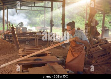 Menuisier qualifié coupant un morceau de bois dans son atelier de travail du bois, charpentiers utilisant la scie circulaire dans l'atelier, style vintage Banque D'Images