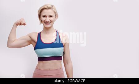 Fille vêtue d'un casque d'activité montrant son biceps. Forte fille posant pour la caméra montrant ses muscles et sa force. Concept de fitness et de gym. Isolé sur fond blanc studio. Banque D'Images