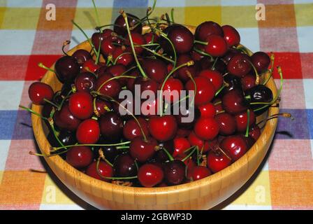 Cerises mûres dans un plateau en bois sur une nappe de couleur Banque D'Images