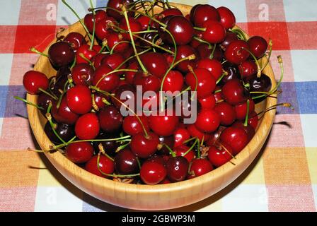 Cerises mûres dans un plateau en bois sur une nappe de couleur Banque D'Images