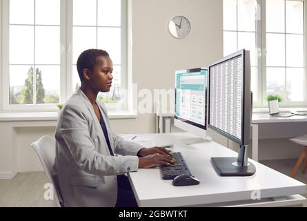 Femme d'affaires ou comptable travaillant avec des documents financiers sur deux ordinateurs de bureau Banque D'Images