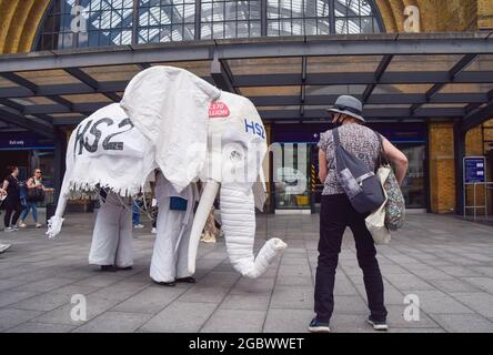 Londres, Royaume-Uni. 05 août 2021. Des manifestants portant un costume d'éléphant blanc « HS2 » sont conduits devant la gare par un autre manifestant pendant la manifestation Stop HS2. Des activistes se sont rassemblés devant la gare King's Cross pour protester contre le nouveau système ferroviaire High Speed 2 (HS2), les écologistes disent qu'ils seront « écologiquement dévastateurs » et qu'ils coûteront 170 milliards de livres sterling aux contribuables. Crédit : SOPA Images Limited/Alamy Live News Banque D'Images